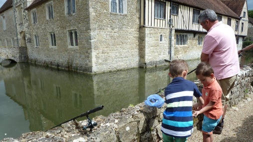 Family visitors fishing in Ightham Mote, Kent with exterior of house in background